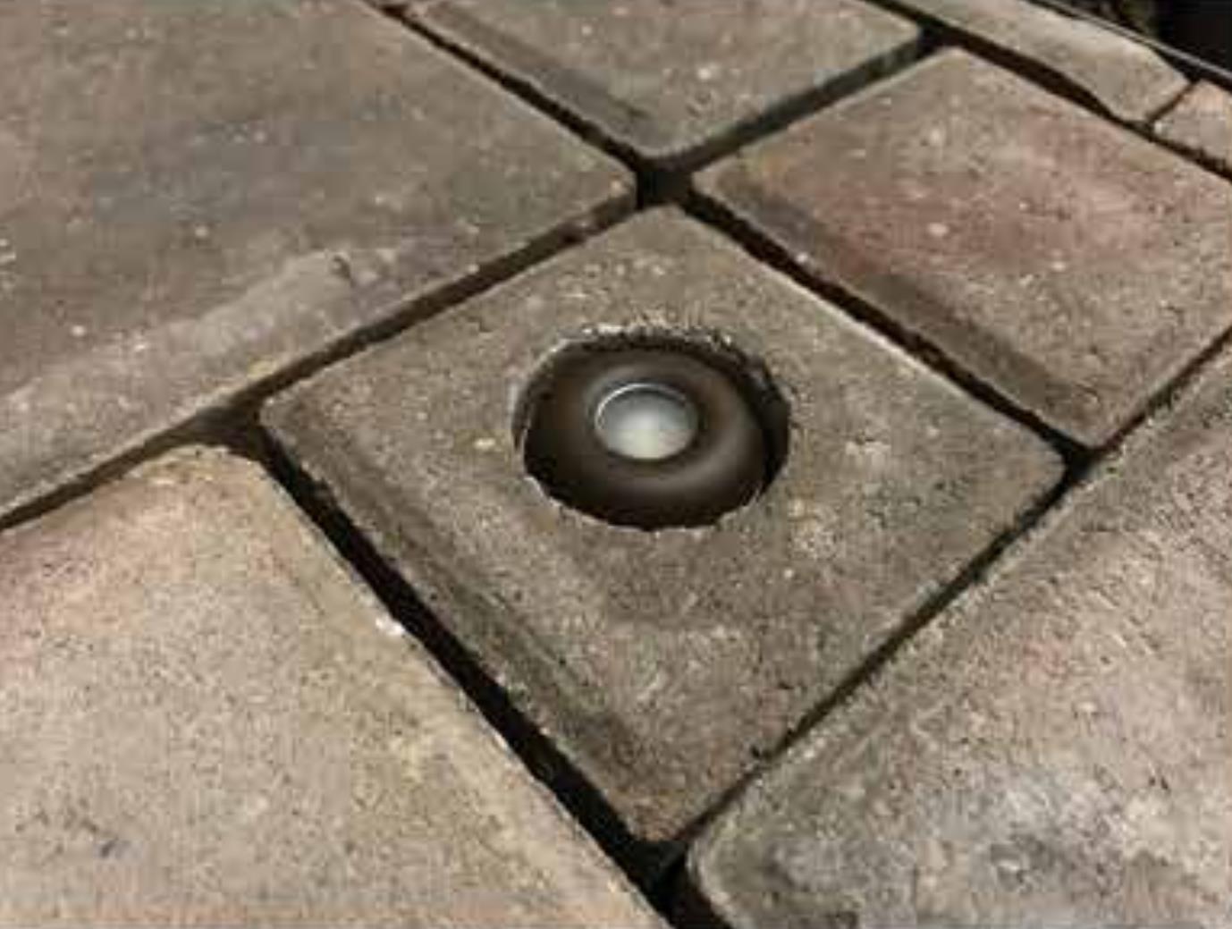 Close-up of the Round Bullet light nestled within a square stone, encircled by larger square stones on a paved surface.