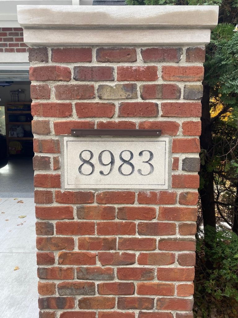 IMG_0834 A brick pillar from the Ledge Bar Series displays a rectangular plaque with the number 8983 mounted on it; a garage entrance is visible in the background.