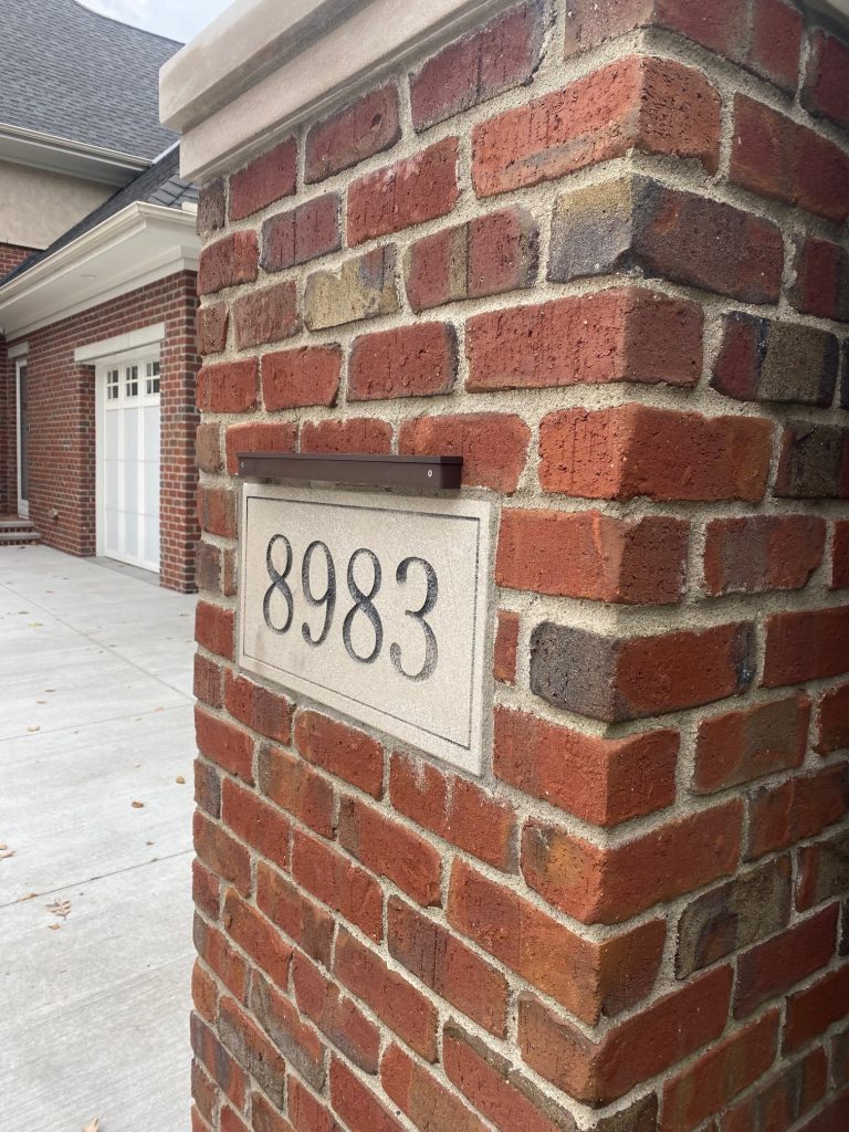 IMG_0836 A brick pillar from the Ledge Bar Series displays the address number 8983 on a rectangular stone plaque near a driveway and a garage.